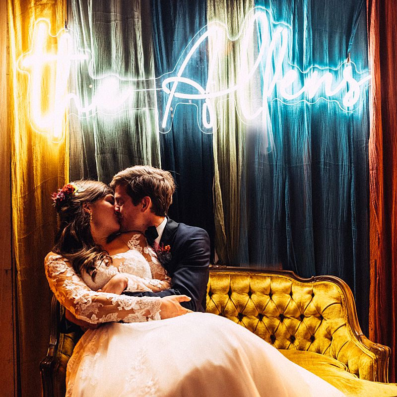 bride and groom kissing in front of custom made sign with their newlywed name in neon at this charleston sc wedding